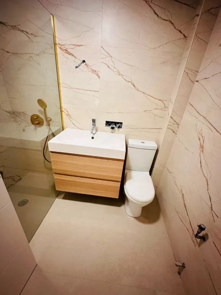 Baño con grifería dorada y ducha de obra en mármol
