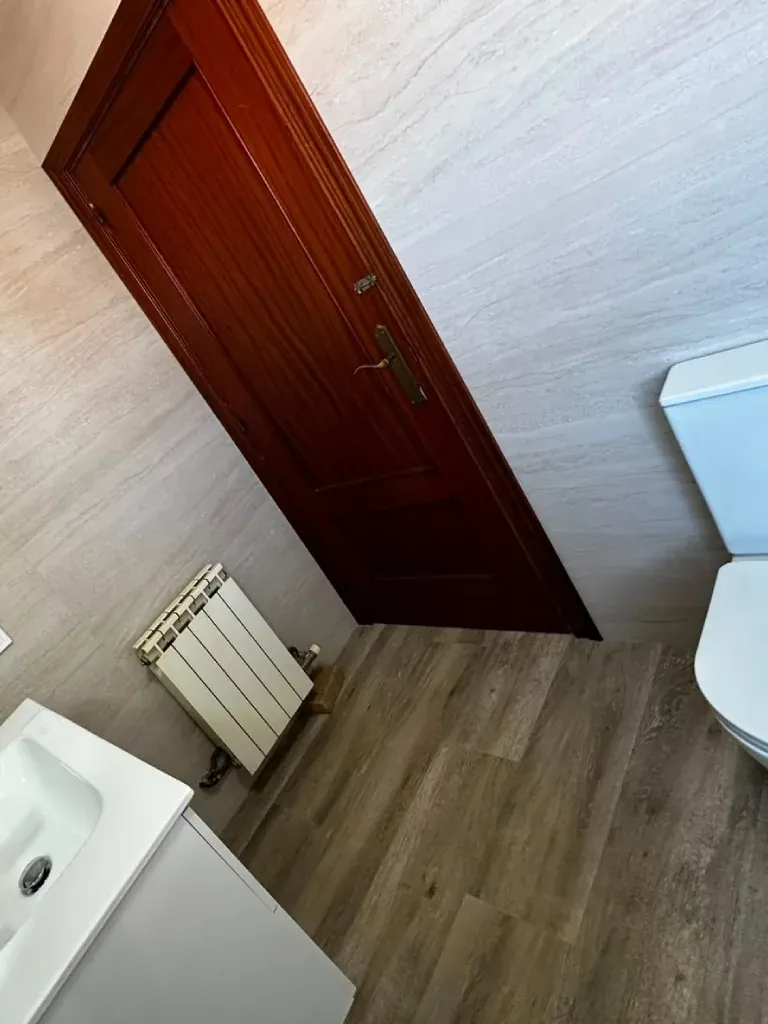 Baño reformado con radiador toallero y suelo laminado